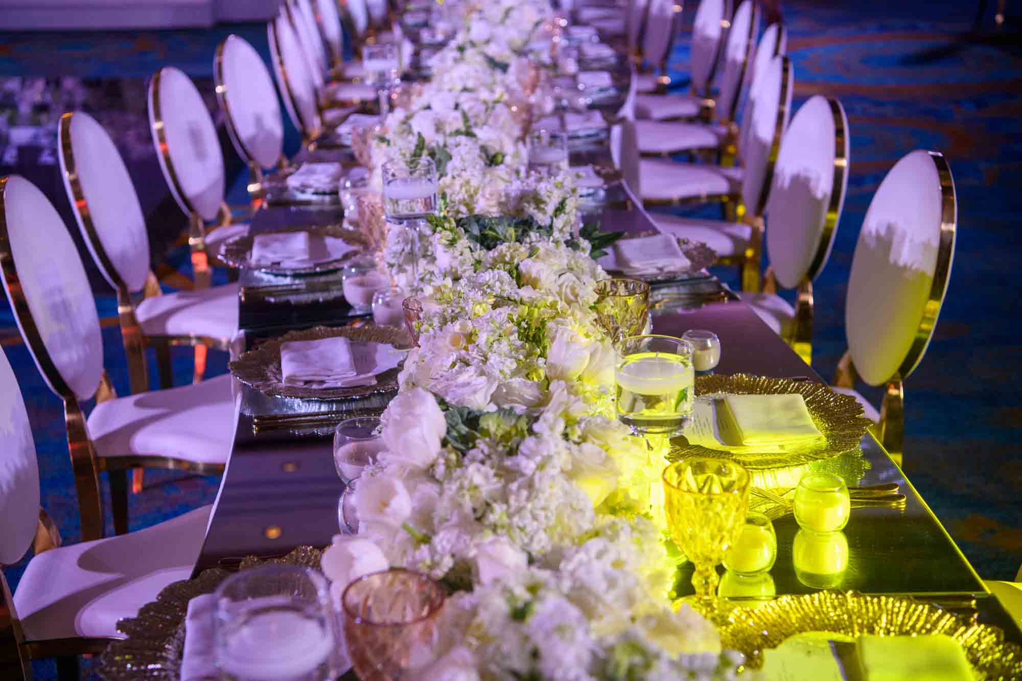 An elongated dining table adorned with white flowers, set for a wedding celebration.