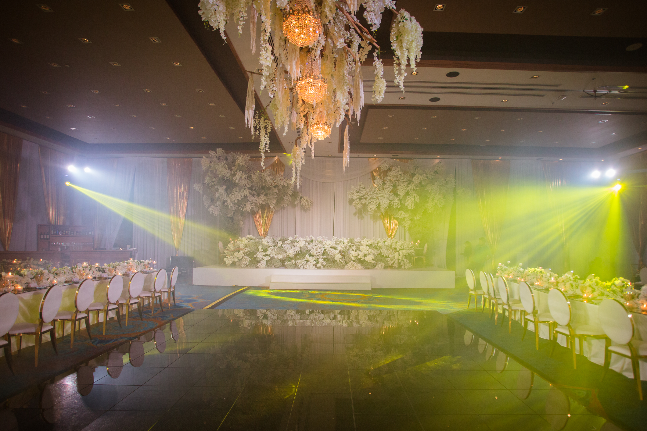 Expansive reception space adorned with white blooms, candles, and yellow party lights for weddings.