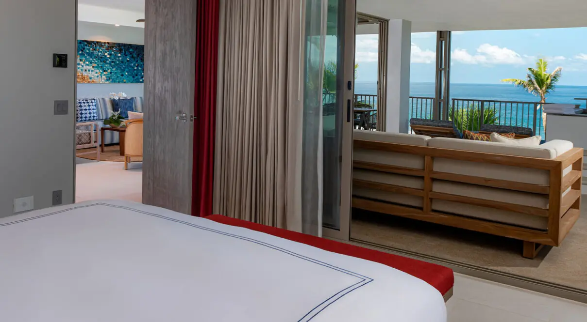 Bedroom opens to outdoor terrace with cushioned sofa, ocean view, palm tree, modern decor, sliding glass doors.