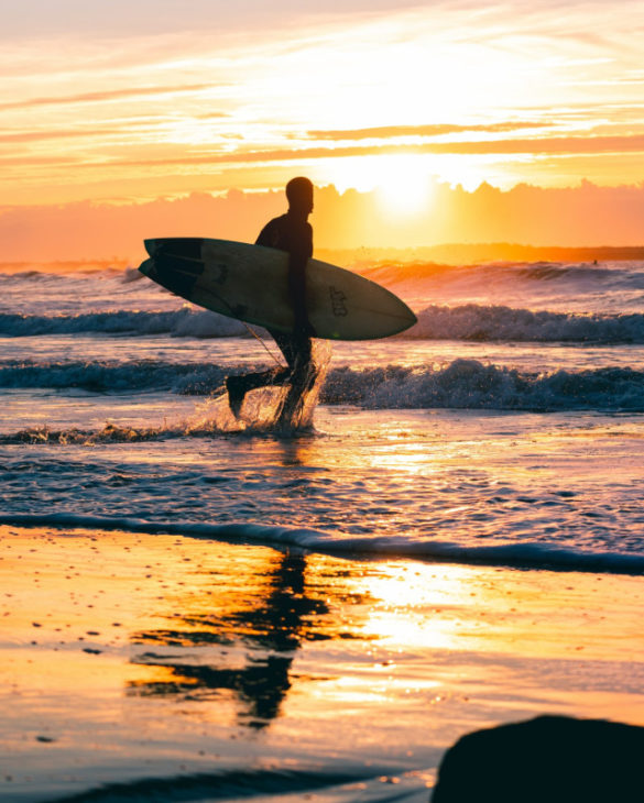 Hombre que sostiene la tabla de surf durante la puesta de sol