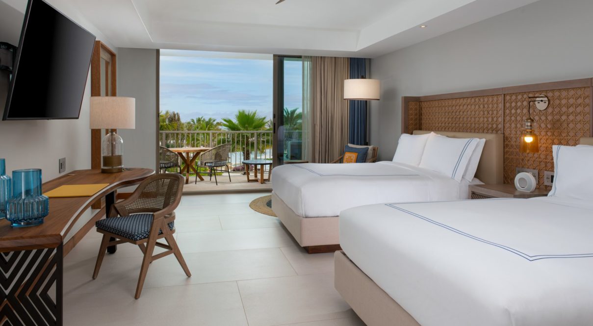 Una habitación de hotel con dos camas, lámparas, tv y silla con vista al río con balcón