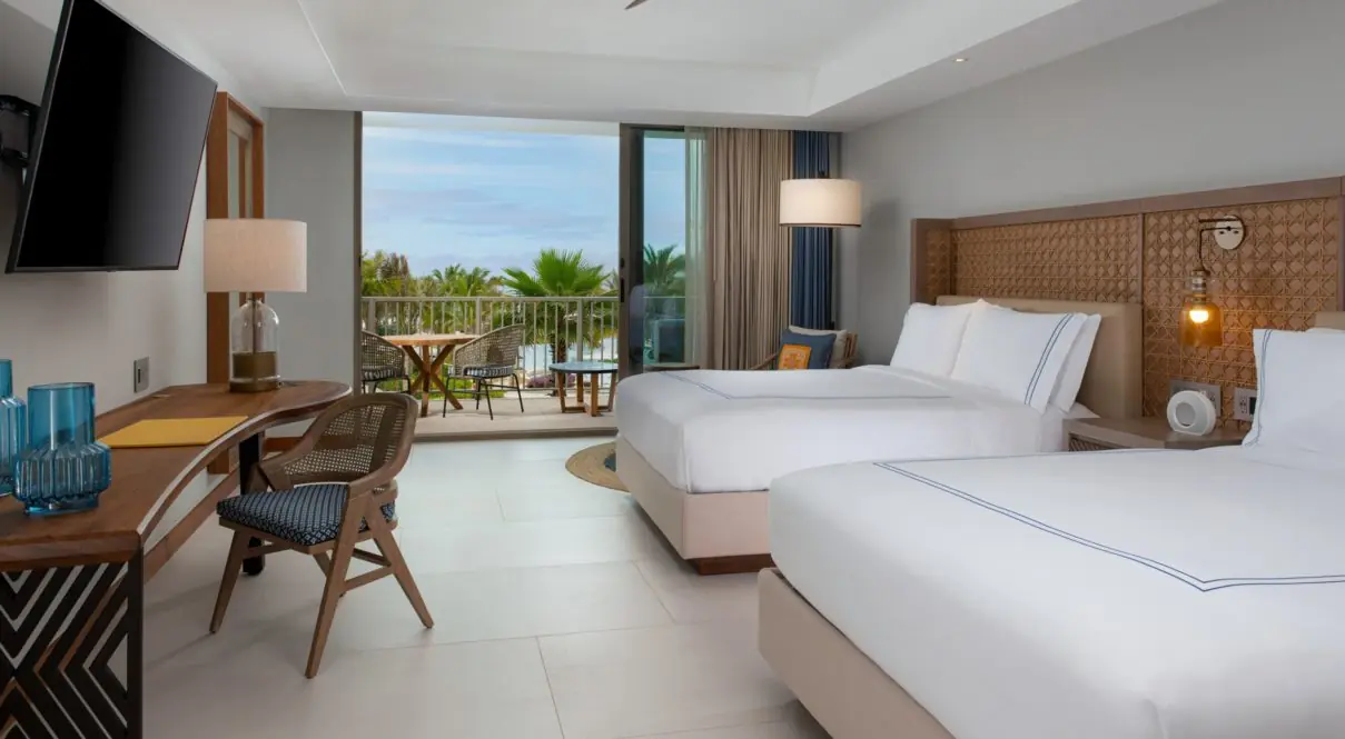 Una habitación de hotel con dos camas, lámparas, tv y silla con vista al río con balcón