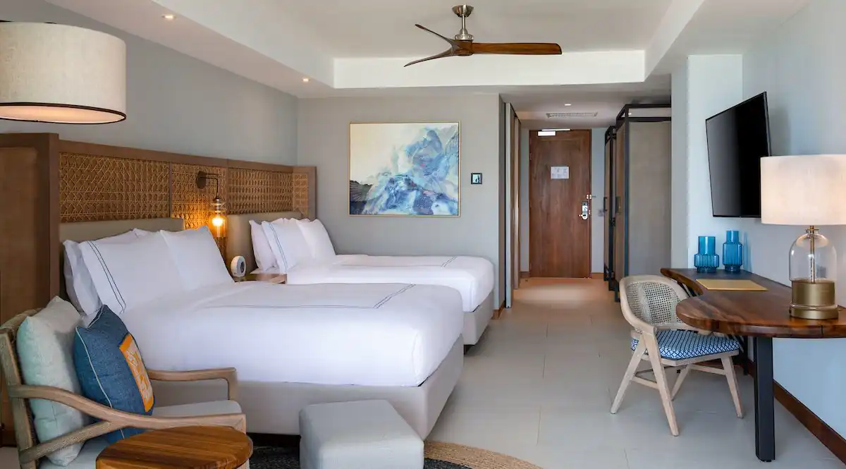 Una habitación de hotel con dos camas, lámparas, cuadros y tv.