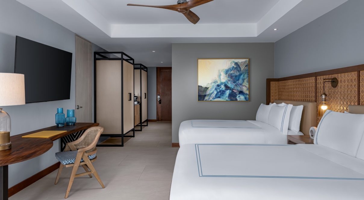 Una habitación de hotel con dos camas, lámparas, tv, pintura y silla.