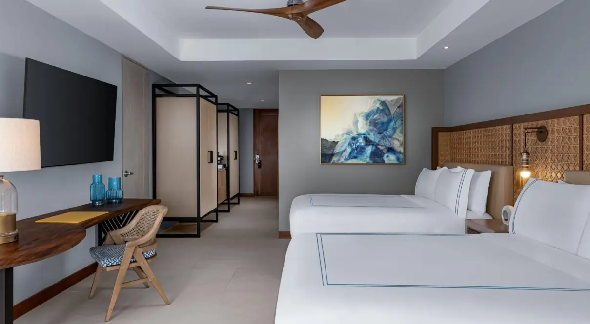 A Hotel room with two beds, lamps, tv, painting and chair