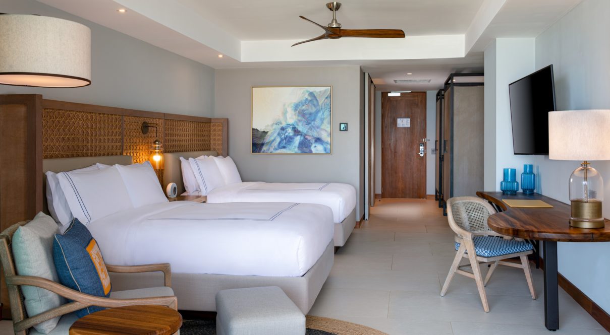 Una habitación de hotel con dos camas, lámparas, tv, pintura y silla.