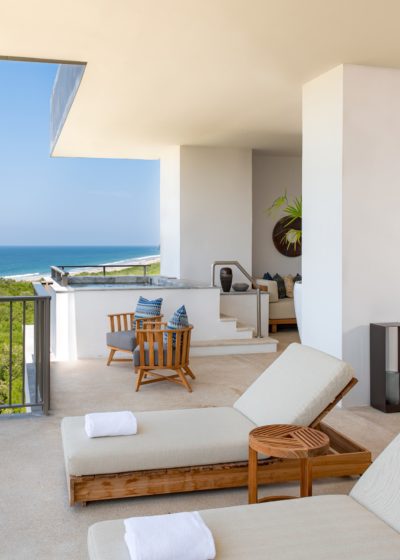 A hotel room balcony with chairs, two swimming pool bed with river view