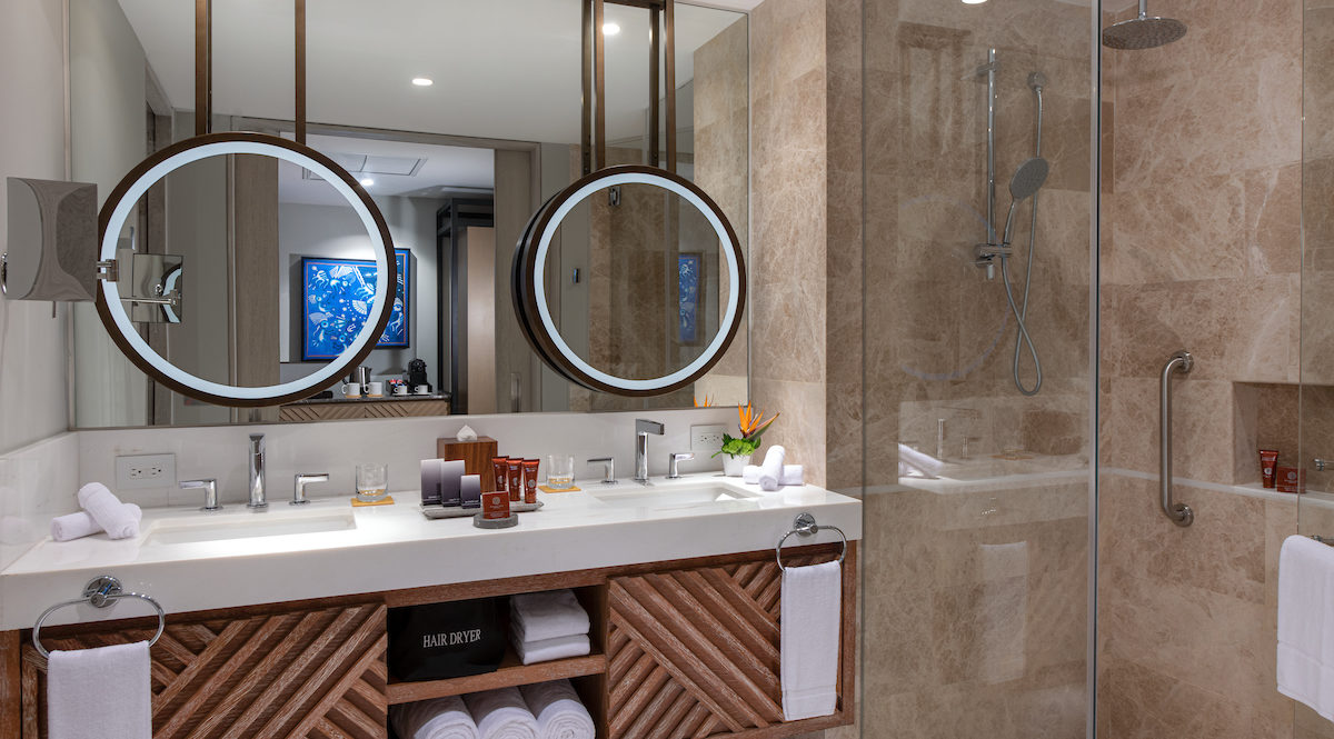 Baño de una habitación de hotel con dos espejos circulares y elementos esenciales