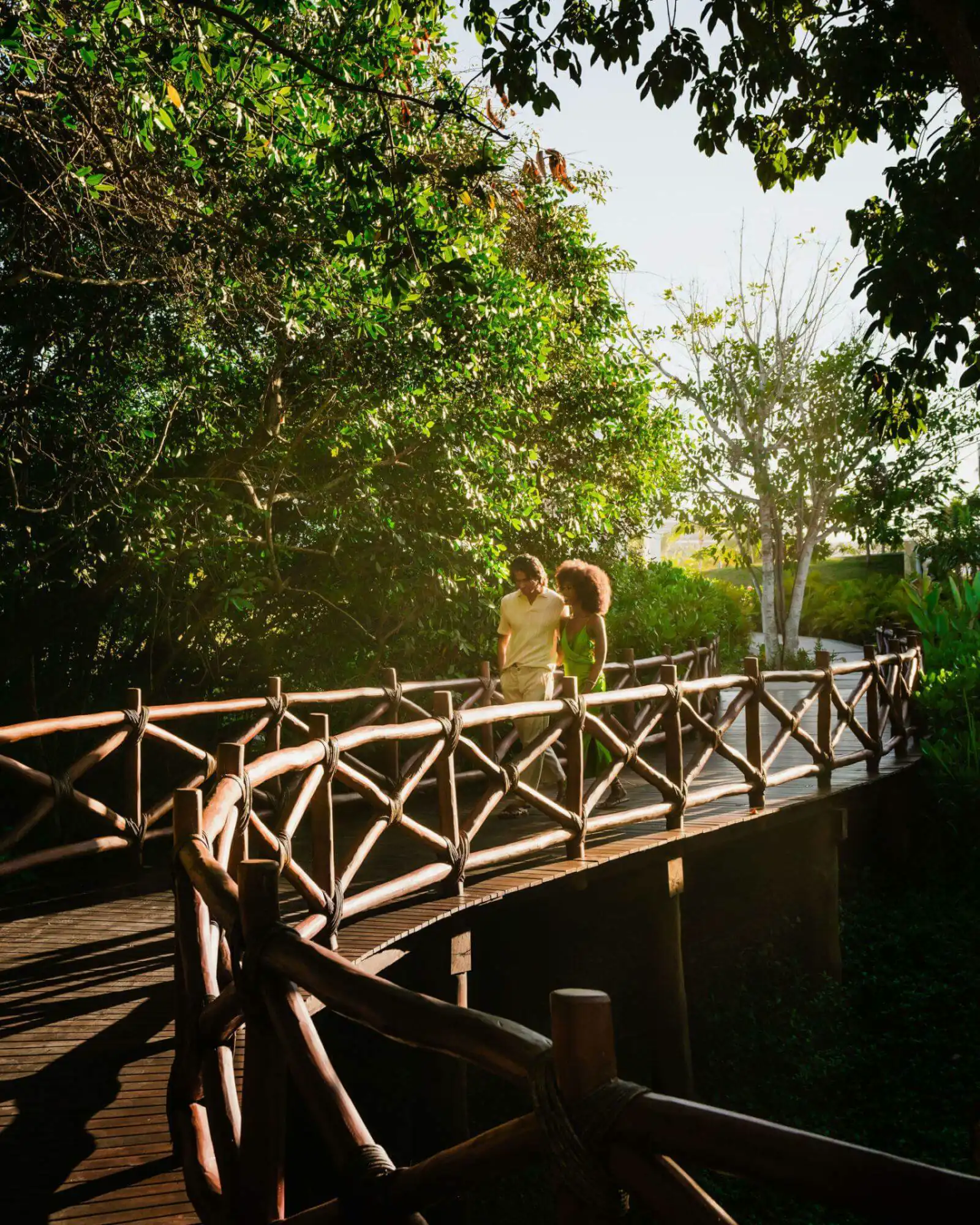 A loving couple walks hand in hand along a forest bridge, surrounded by nature.
