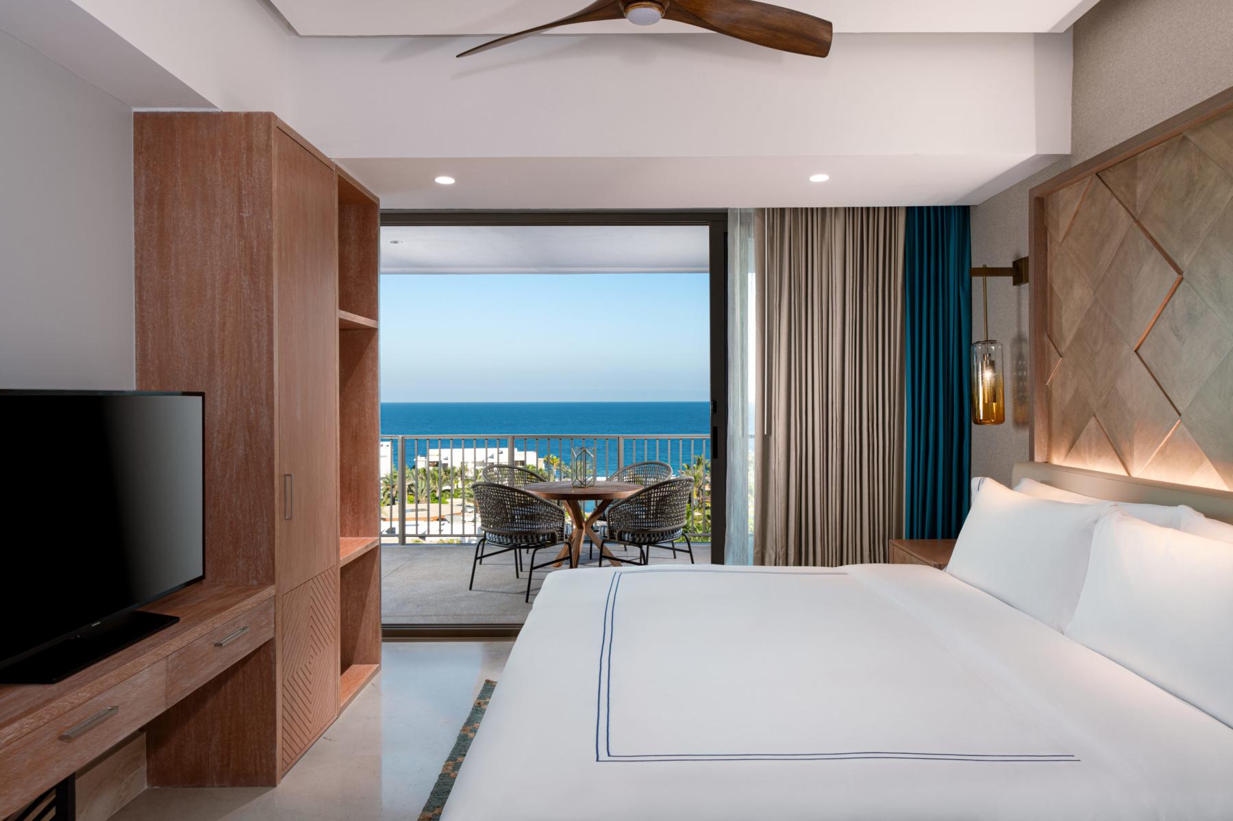 Una habitación de hotel con cama, tv y lámpara brillante con vista al río con balcón