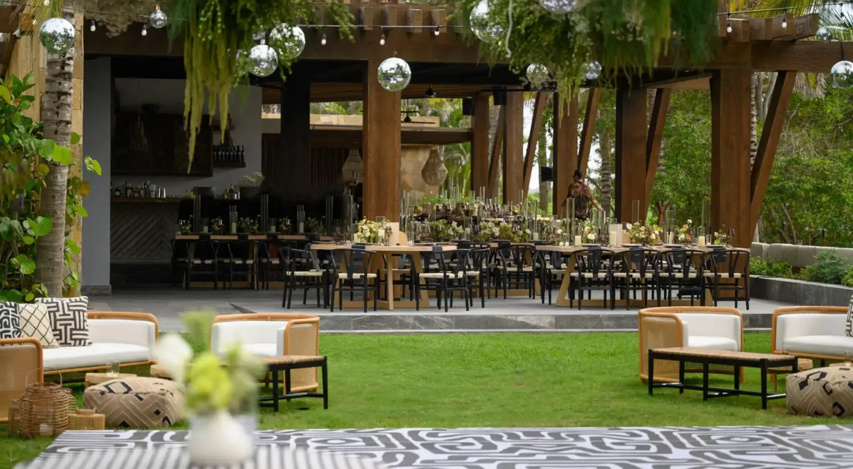 Modern outdoor event setup with black chairs, floral décor, disco balls, patterned tables, and cozy lounge seating.
