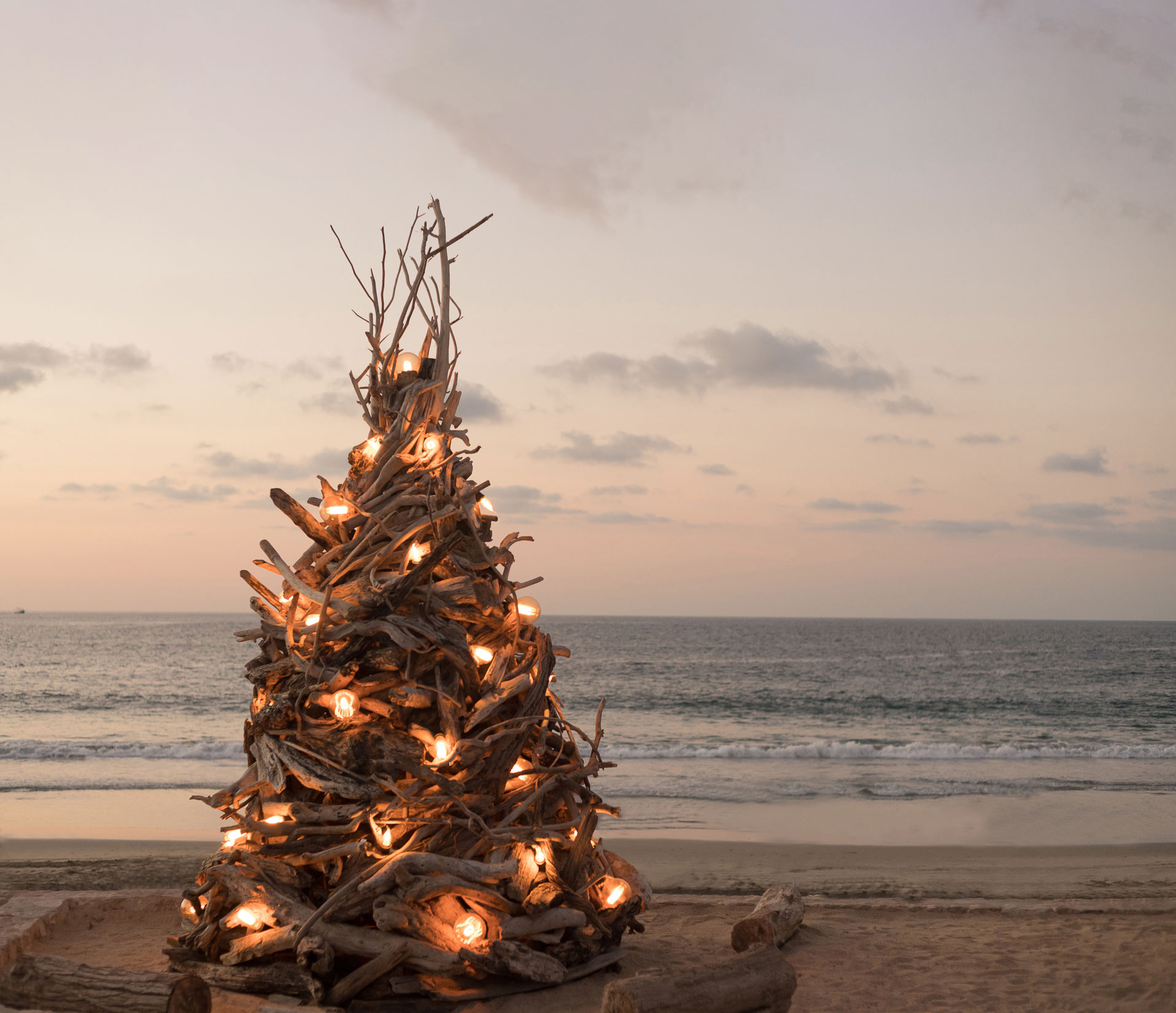 A wooden branch Christmas tree at the beach glows beautifully with several candles.