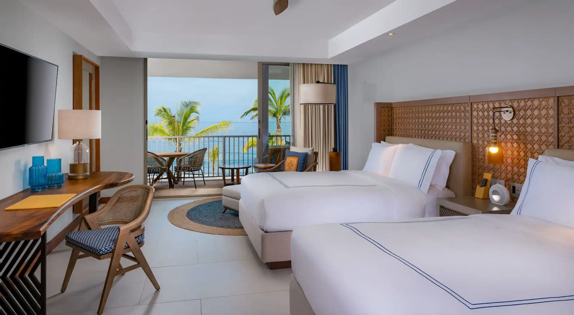 Habitación de hotel con dos camas y una silla y una vista impresionante del océano desde el balcón