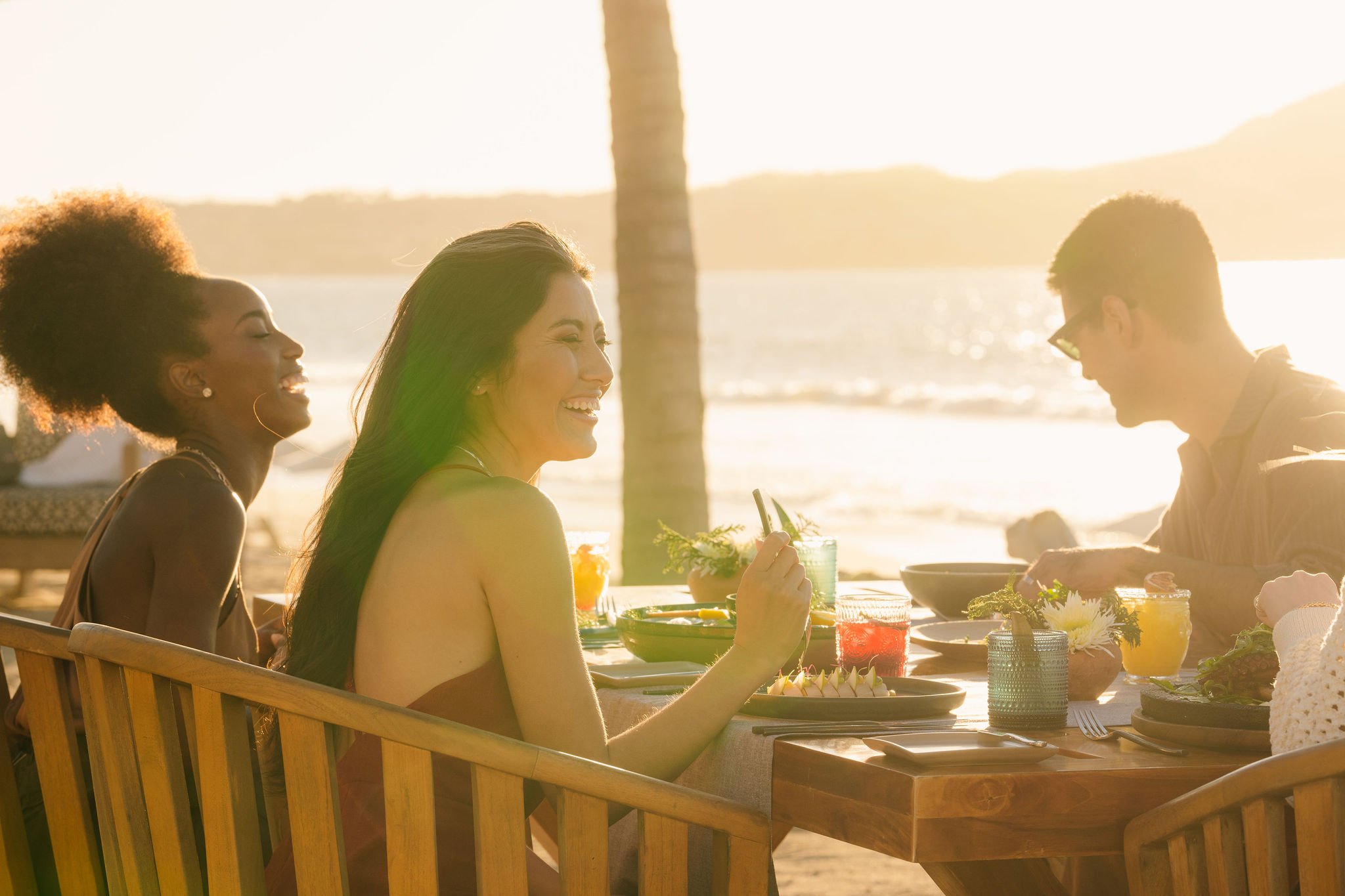 Two women and a man savor breakfast by the seaside in the morning sun.