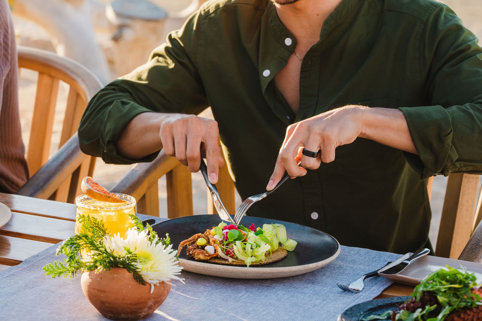 A man in a dark green shirt uses a knife and fork to cut breakfast.