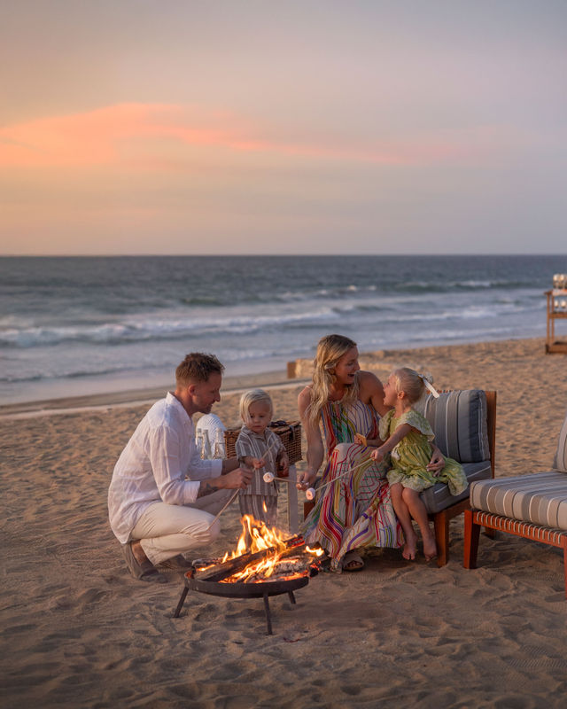 Una familia se sienta en la playa cerca de una fogata, asando malvaviscos durante una hermosa puesta de sol.