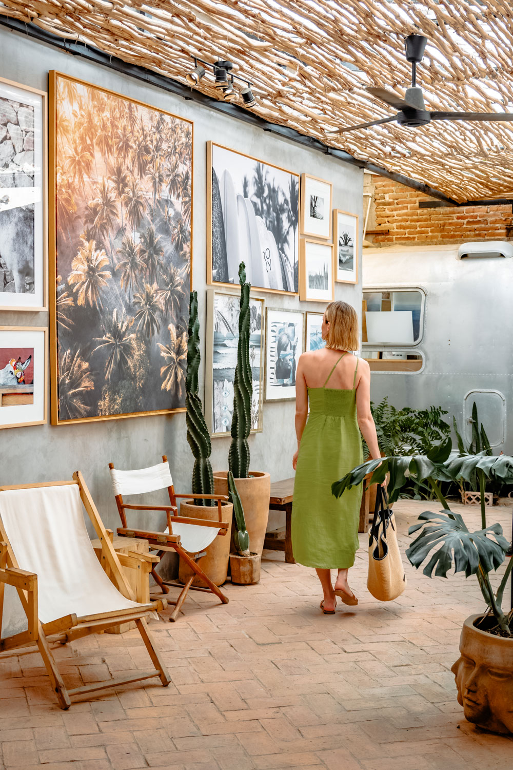 Una mujer con un vestido verde se encuentra dentro de un salón moderno con plantas de cactus y arte de pared enmarcado.
