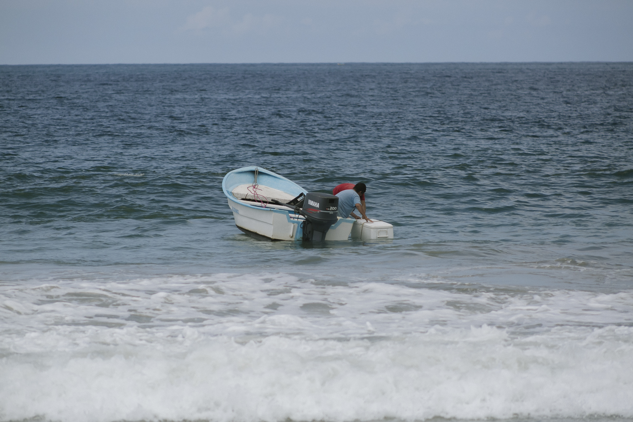 Two men anchor their boat in the ocean, peering intently into the water.