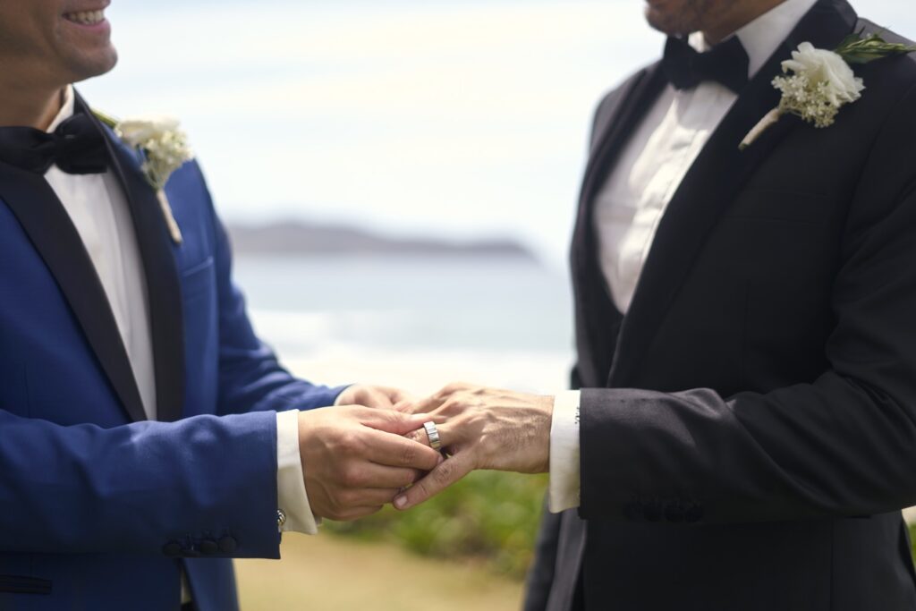 Two men are engaging while wearing rings, symbolizing a commitment or partnership.
