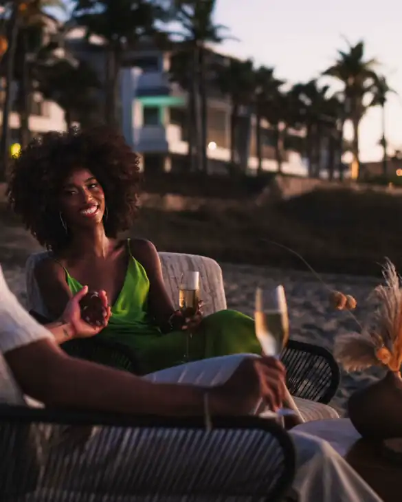 Una pareja de playa en un sofá, con las manos entrelazadas, saboreando bebidas junto a la orilla.