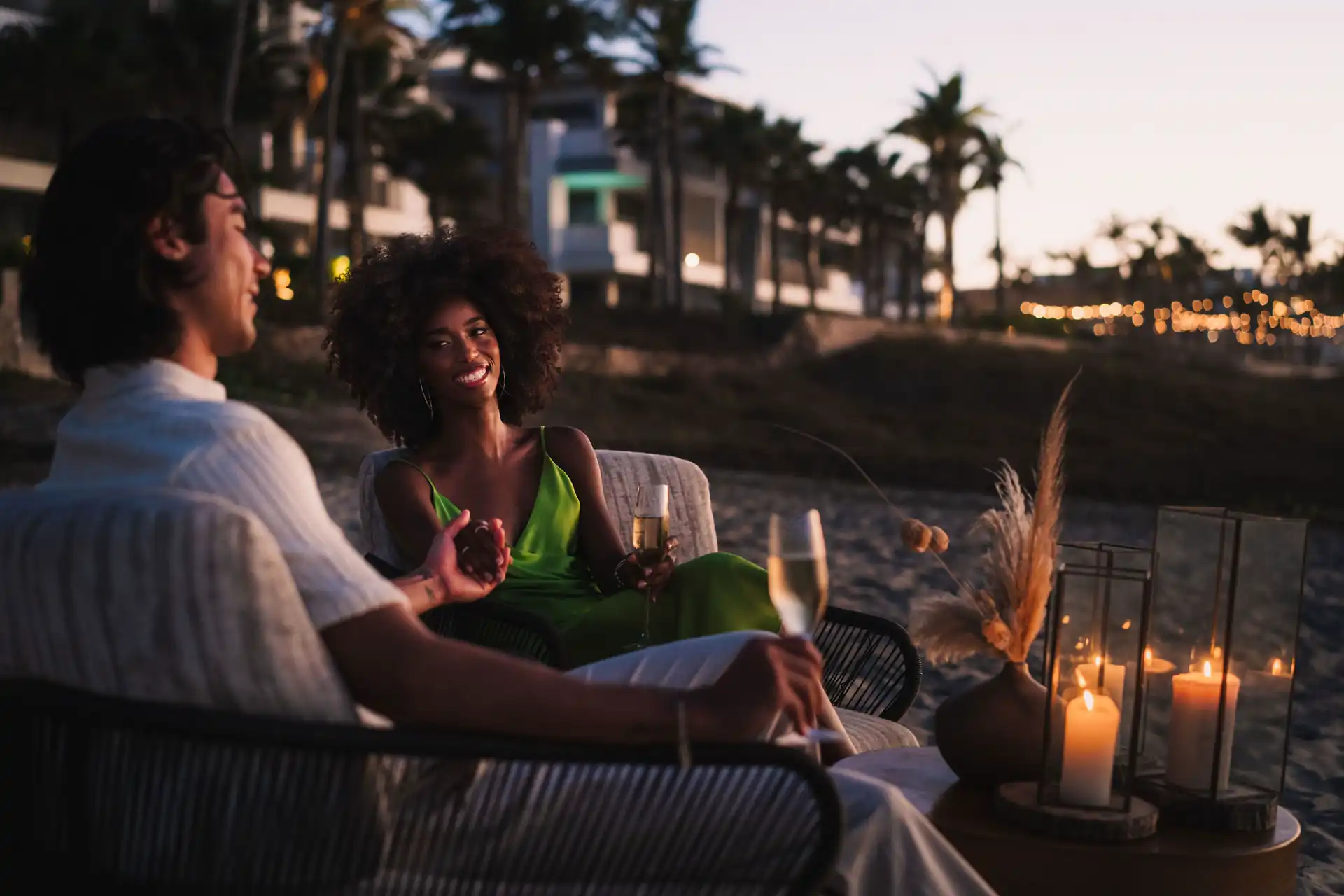 Una pareja de playa en un sofá, con las manos entrelazadas, saboreando bebidas junto a la orilla.