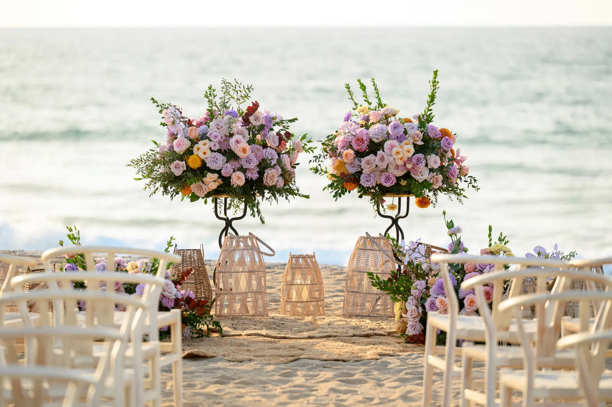 Una configuración de boda incluye dos jarrones de flores largos en la playa, mostrando una impresionante vista al mar.