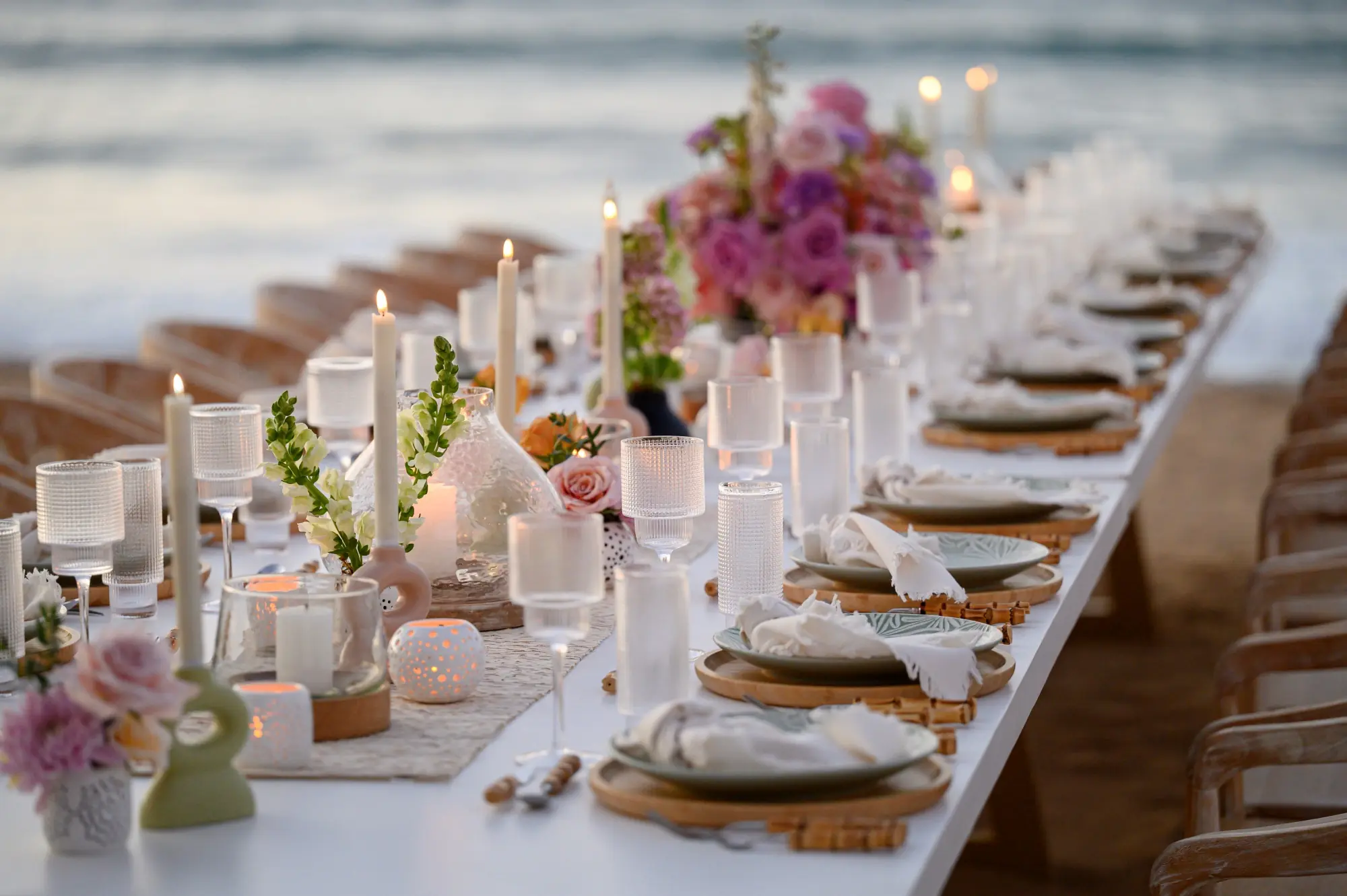 A long table is elegantly decorated with flowers, candles, and crockery for the celebration.