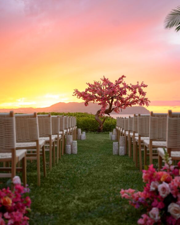 Una hermosa configuración de boda frente a un árbol de flores rosas, con impresionantes vistas al amanecer y al mar.