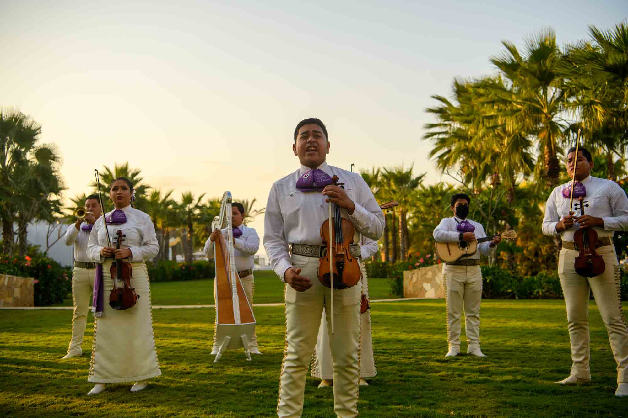 A wedding band is performing with instruments while singing on the lush lawn.