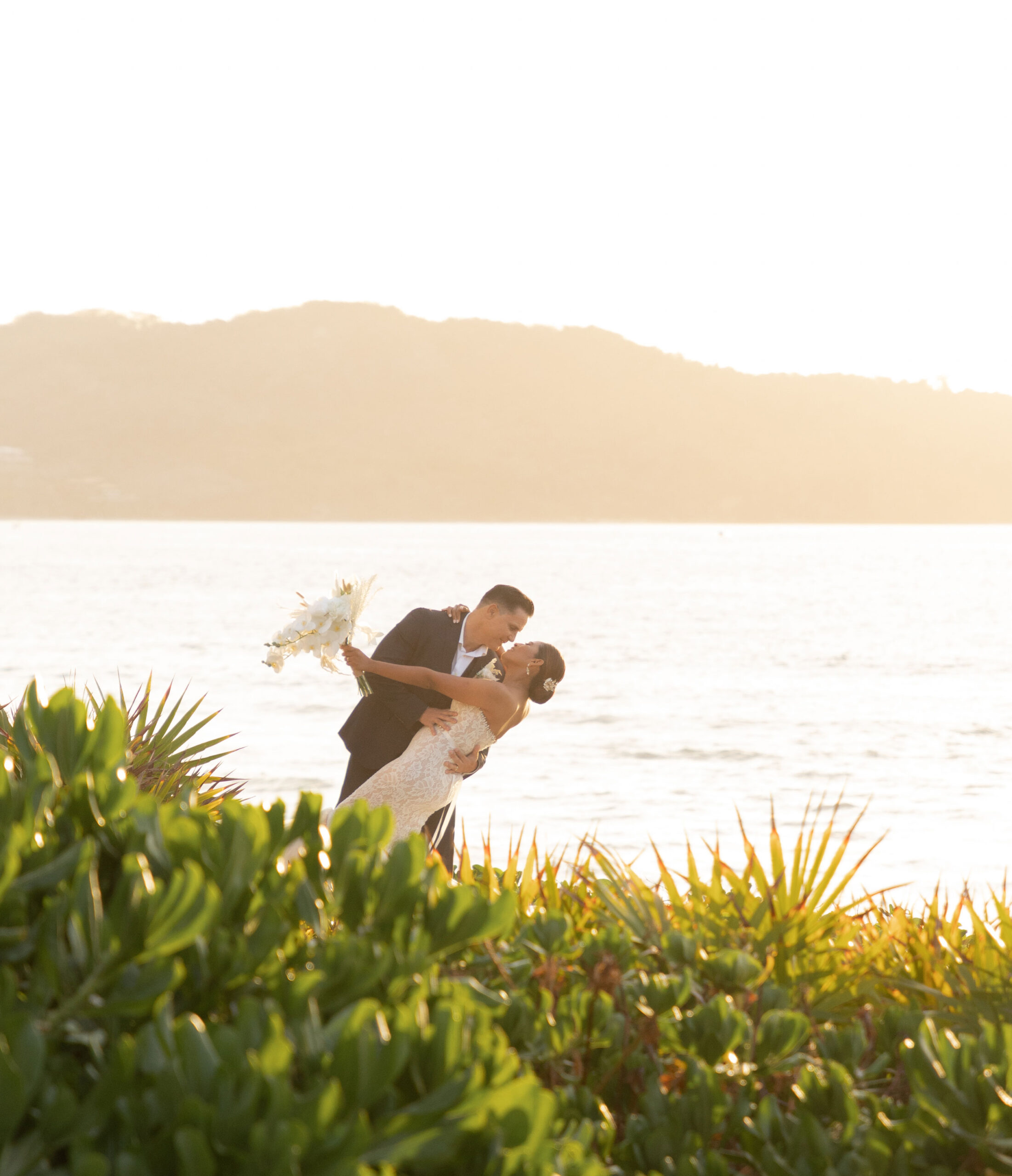 A wedding couple shares a kiss on the beach, with a stunning sea view.