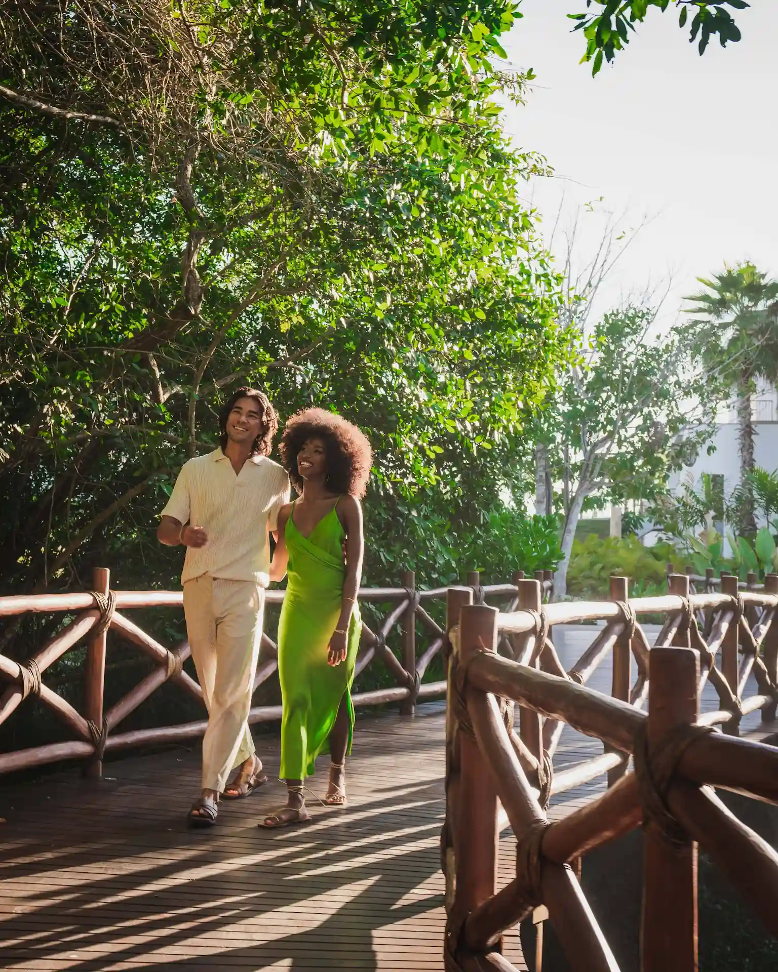Couple walking along a sunlit wooden path surrounded by lush greenery, capturing the resort’s serene atmosphere.
